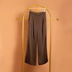 A still image of brown satin straight leg pant on a hanger against an orange wall.