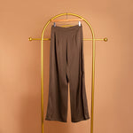 A still image of tan satin straight leg pant on a hanger against an orange wall. 