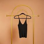 A black rib-knit tank top on a hanger against a orange background. 