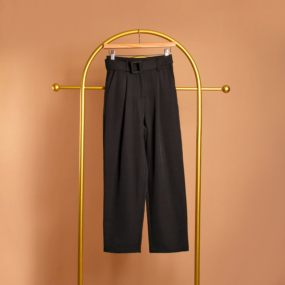 A still image of a black straight leg pant on a hanger against an orange background. 