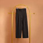 A still image of a black straight leg pant on a hanger against an orange background. 