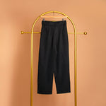 A still image of a black straight leg pant with a belt on a hanger against an orange background. 