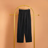 A still image of a black straight leg pant with a belt on a hanger against an orange background. 