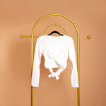 A still image of a white front cross back tie top on a hanger against an orange background. 