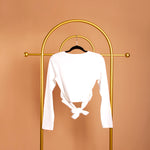 A still image of a white front cross back tie top on a hanger against an orange background. 