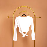 A still image of a white front cross back tie top on a hanger against an orange background. 