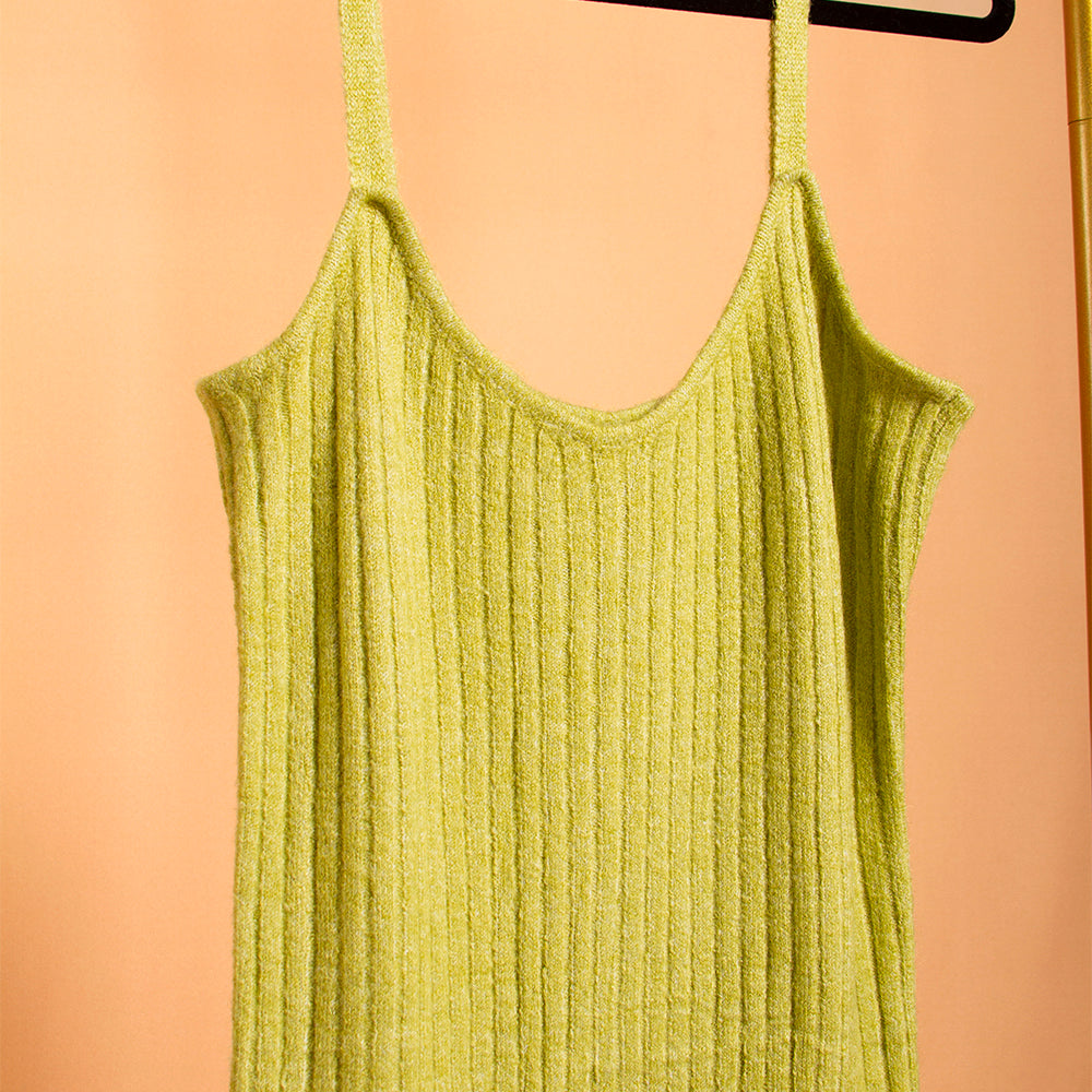A still detailed image of a green midi rib knit dress on a hanger with an orange background. 