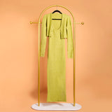 A still image of a green two piece set of a cardigan and midi dress on a hanger with a orange background. 