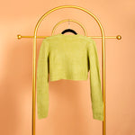 A still image of a green rib knit cardigan from the backside view on a hanger against an orange background. 