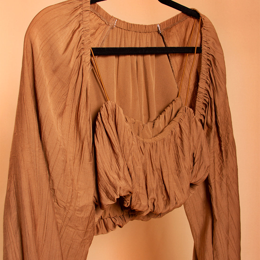 A still image of a woven crop top and shrug set on a hanger against a orange wall. 