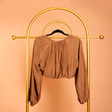 A backside view image of a woven shrug on a hanger against a orange wall. 