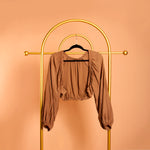 A still image of a woven shrug on a hanger against a orange wall. 