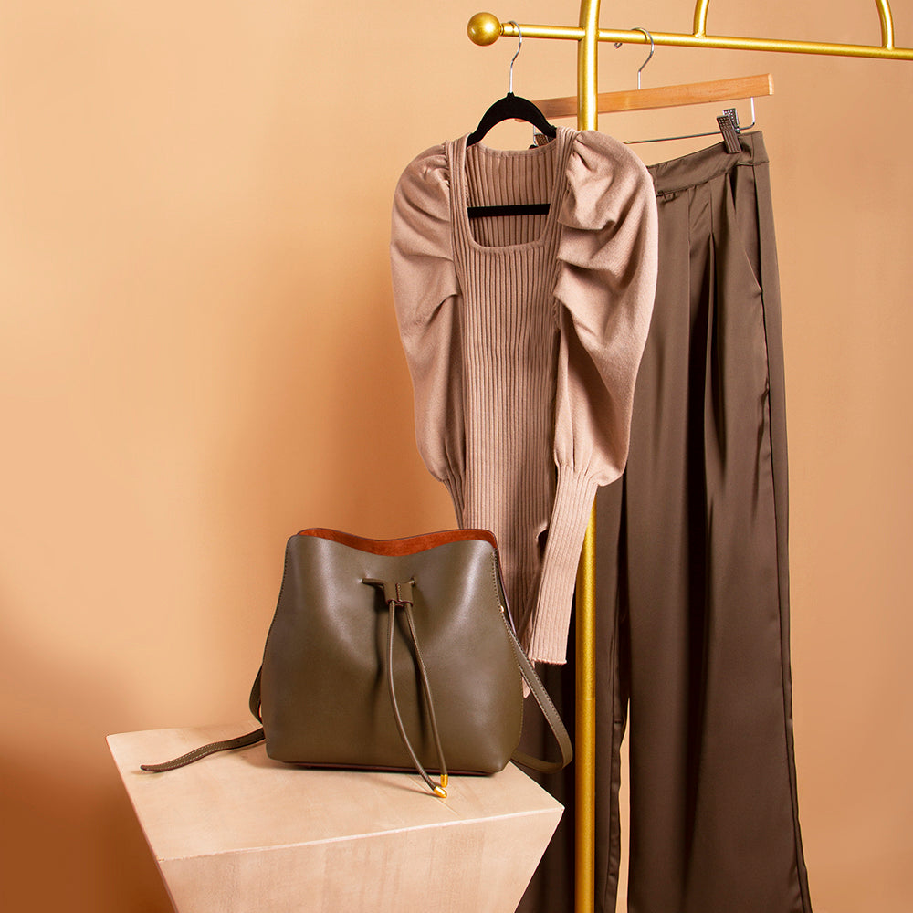 A still image of a vegan leather bag, a puff sleeve bodysuit, and sating straight leg pant against an orange wall. 