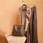 A still image of a vegan leather bag, a puff sleeve bodysuit, and sating straight leg pant against an orange wall. 