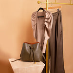 A still image of a puff sleeve bodysuit with brown pants on a hanger with a vegan leather bag in front. 