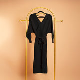 A still image of a black wrap knit midi dress on a hanger against an orange background. 
