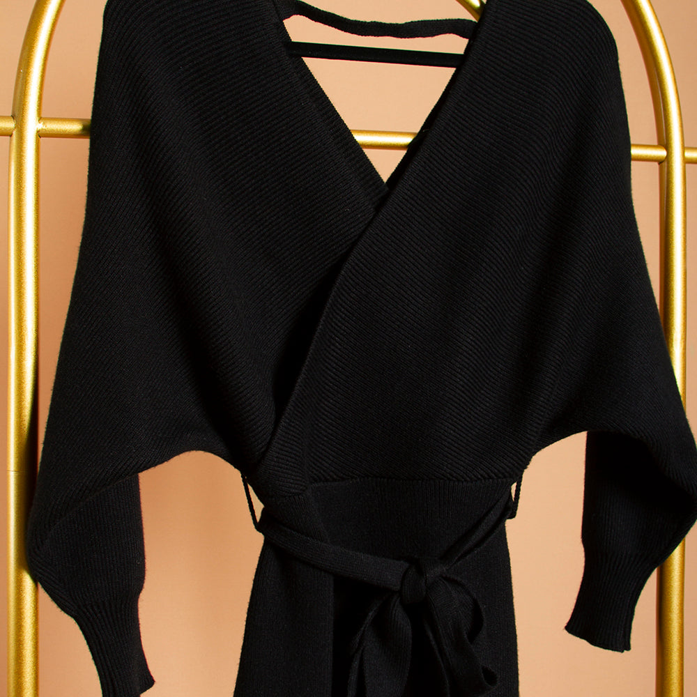 A detail image of a black wrap knit midi dress on a hanger against an orange background. 