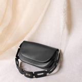 A still image of a black recycled vegan leather shoulder bag with a scallop strap against a sheet. 