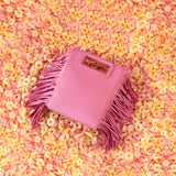 A still image of a square structured pink crossbody bag with fringe laying in candy.