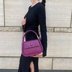  A model wearing a structured vegan leather crossbody bag with double handles against a concrete.