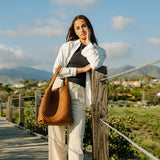 A model wearing a large woven vegan leather shoulder bag outside on a boardwalk. 
