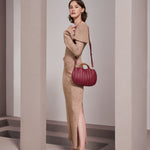 A model wearing a small burgundy vegan leather crossbody bag with pleated detail and wooden handle.