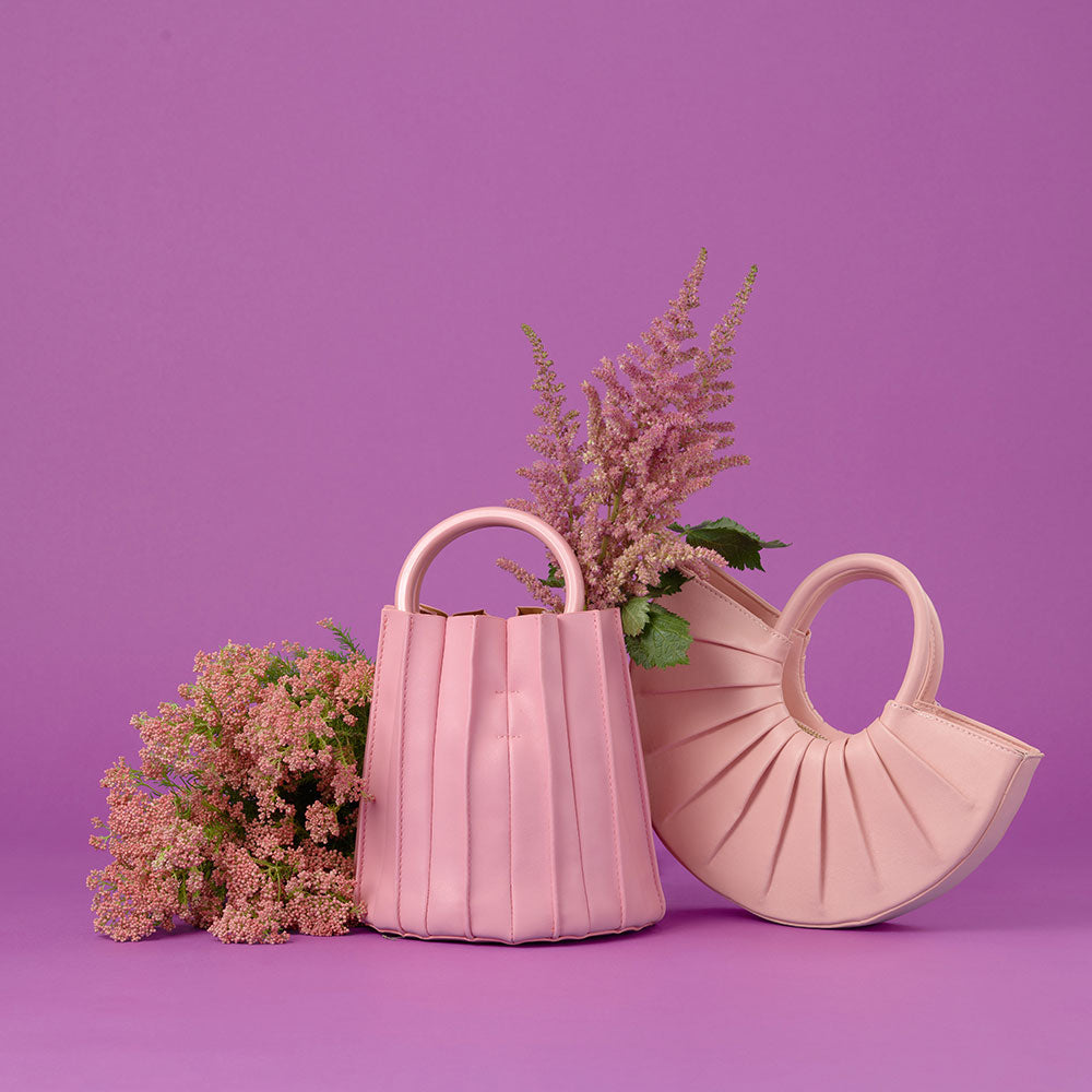 A still image of two pink vegan leather bags with flowers on the ground against a purple background. 