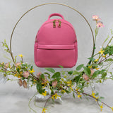 A still image of a pink recycled vegan leather shoulder bag with a gold ring around the bag with yellow and pink flowers around the bag.