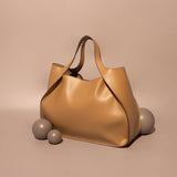 A still image of a large recycled vegan leather tote bag with a wrapped handle against a tan wall. 