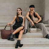 Two models holding multiple recycled vegan leather handbags while sitting on stiars. 
