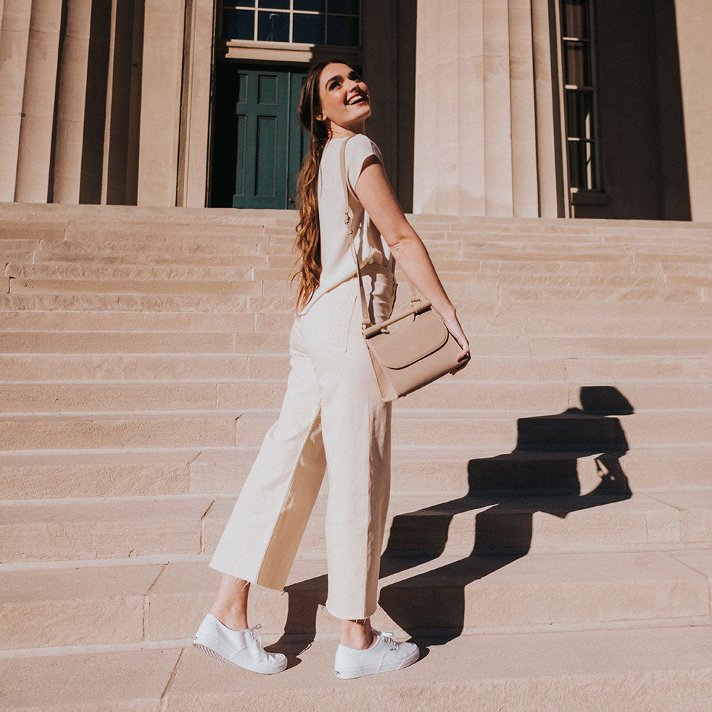 A model wearing a small square structured vegan leather crossbody bag against stairs.