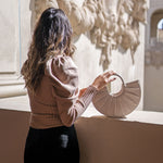 A model wearing a tan puff sleeve knit bodysuit against a wall with a vegan leather handbag.