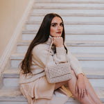 A model wearing a small crocheted vegan leather shoulder bag sitting on stairs. 