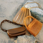 A still image of three different handbags laying against sand and rocks. 