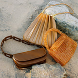 A still image of three different handbags laying against sand and rocks. 