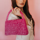 A model wearing a crystal beaded top handle bag with a flap closure against a pink wall. 