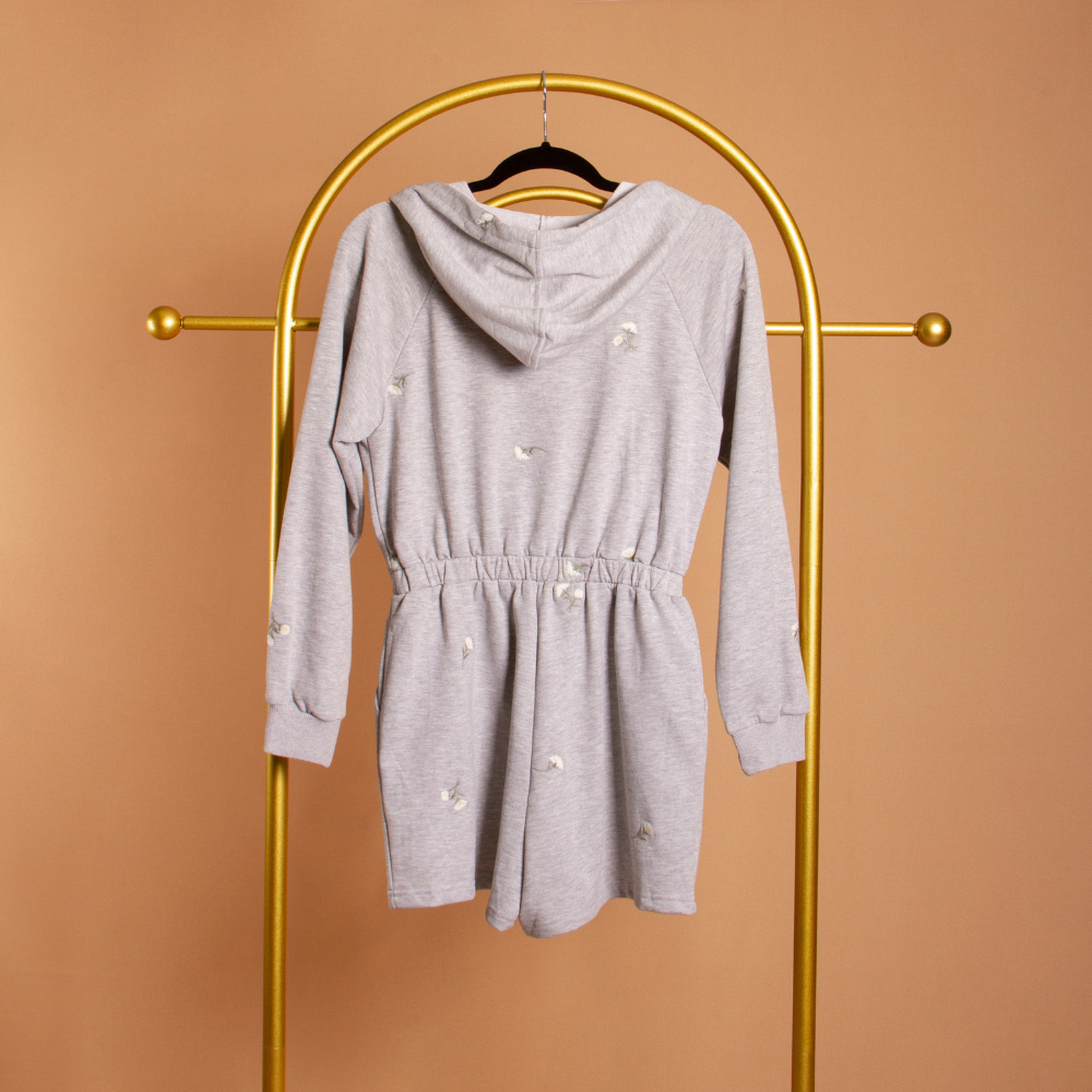 A grey terry hooded romper on a hanger against an orange wall. 
