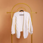 A still image of a white knitted cardigan on a hanger against an orange wall.