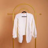 A still image of a white knitted cardigan on a hanger against an orange wall.