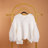 A still image of a white knitted cardigan backside view on a hanger against an orange background. 