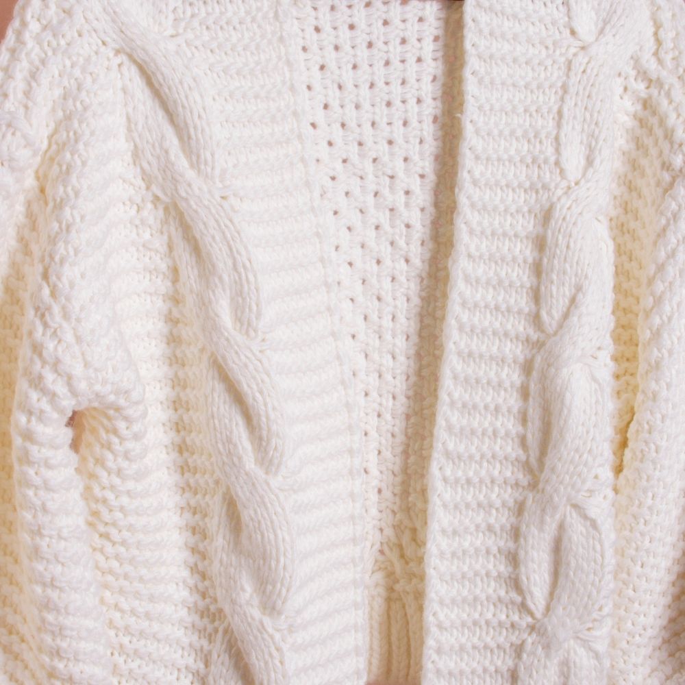 A still detail image of a white knitted cardigan. 