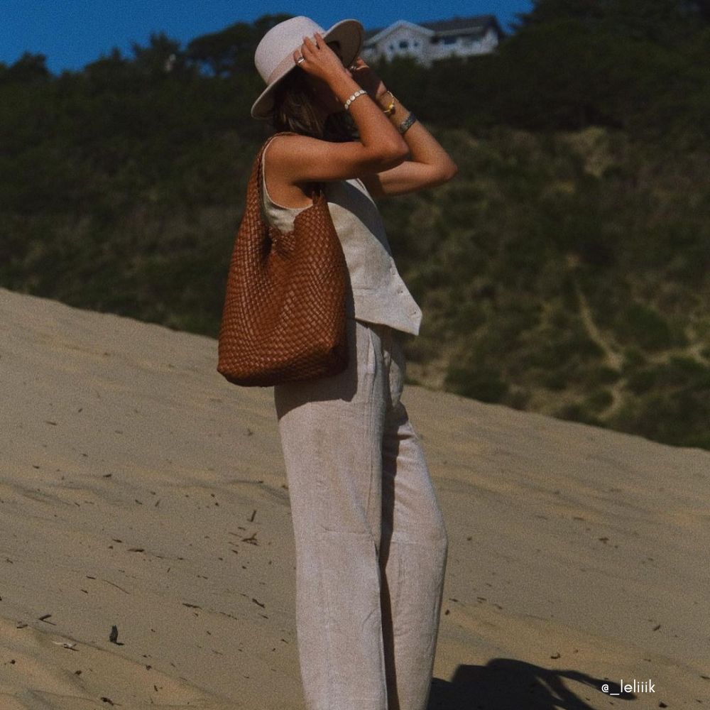 A model wearing a large woven vegan leather shoulder bag on the beach.