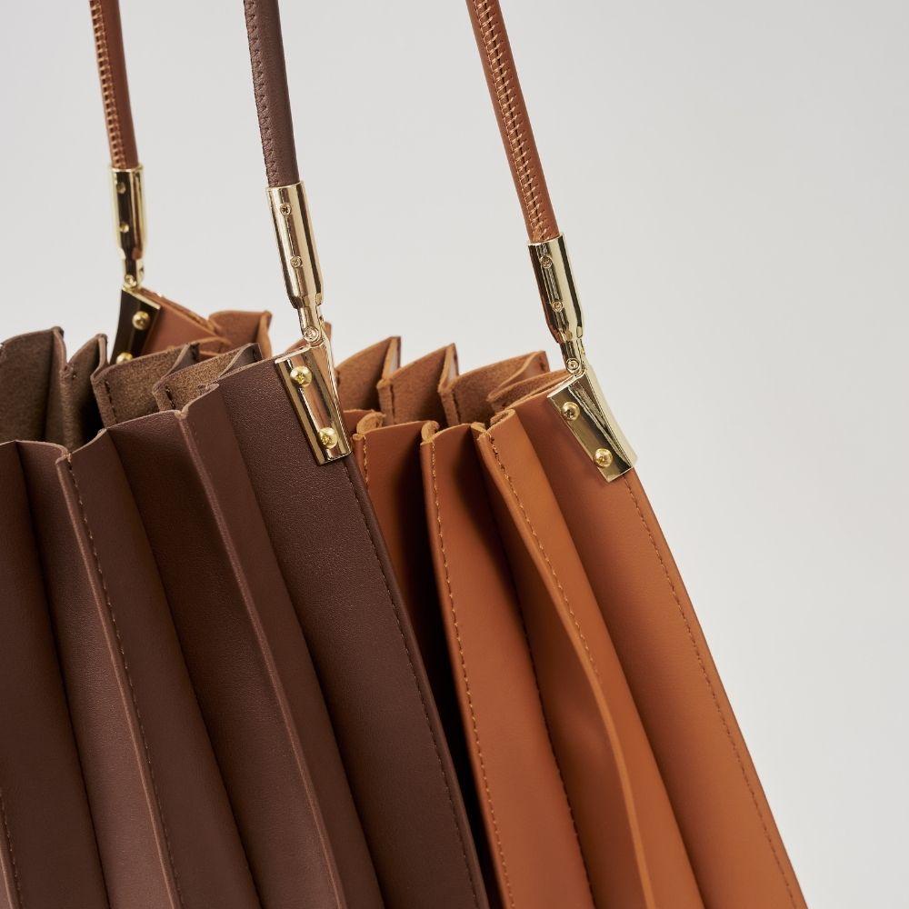A detail photo of a pleated vegan shoulder bag with gold hardware.