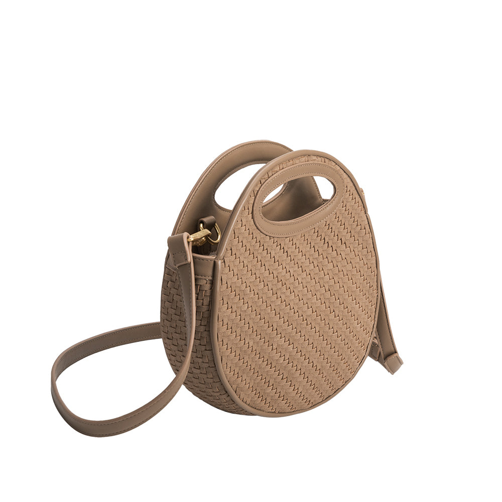 A taupe circle shaped vegan leather crossbody bag with woven pattern.