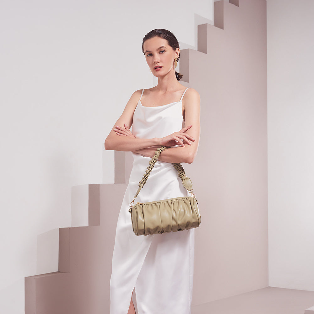 A model wearing a medium moss cylindrical-shaped shoulder bag with a ruched body and strap against a white background. 