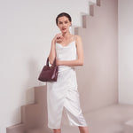 A model wearing a small burgundy recycled vegan leather crossbody handbag against a white background. 