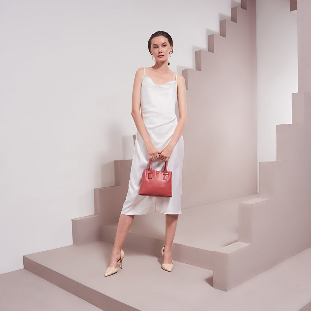 A model wearing a small recycled vegan leather crossbody handbag against a tan wall. 
