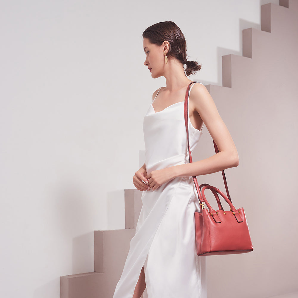 A model wearing a small rose recycled vegan leather crossbody handbag against a tan wall. 