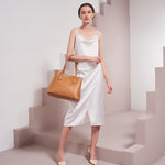 A model wearing a large vegan leather shoulder bag with gold hardware against a white wall. 