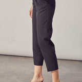 A model wearing a black straight leg pant with a belt against a white wall. 